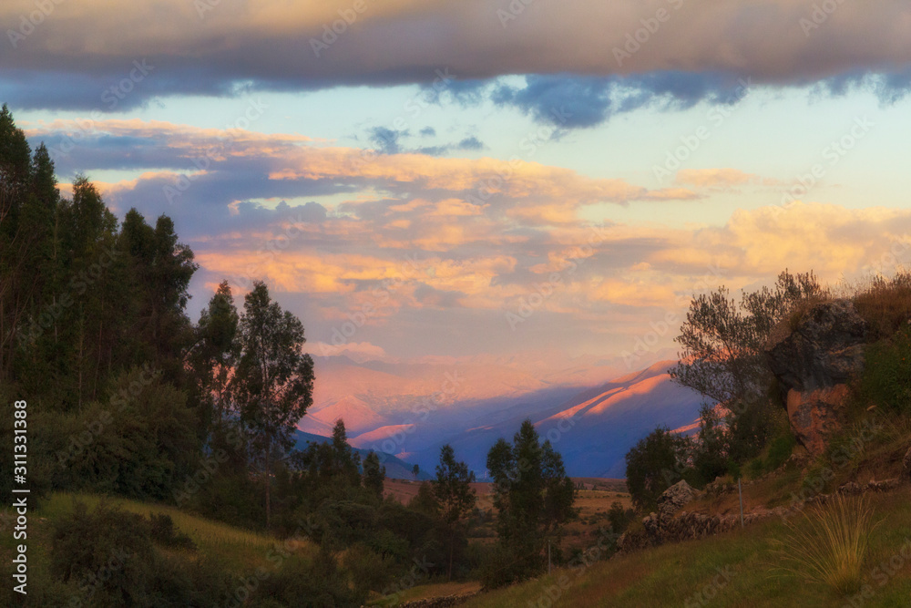 A sunset that is a making a valley and the clouds above at Sacsayhuaman, Peru, glow.