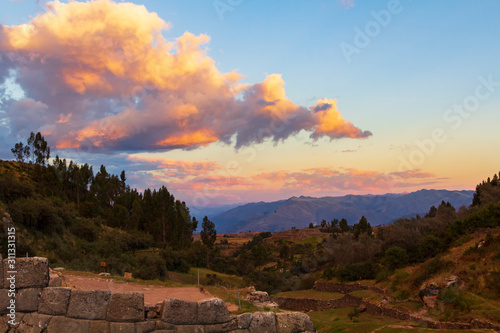 A sunset that is a making a valley and the clouds above at Sacsayhuaman, Peru, glow.
