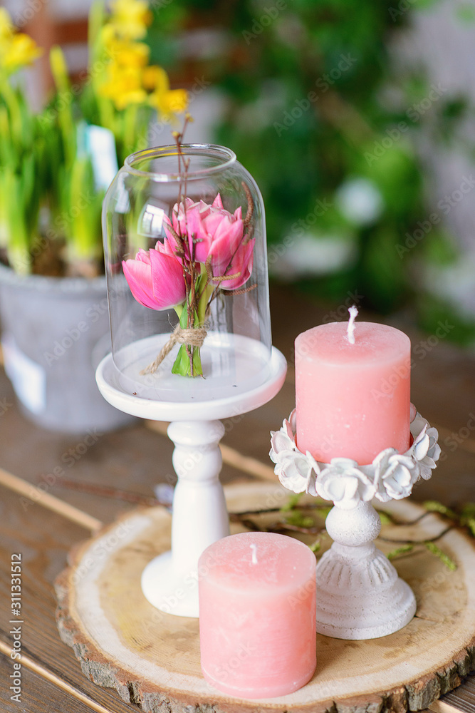 Mini bouquet of fresh flowers tulips under a glass cover on a white metal stand on a wooden stand. Floral decoration of a festive wedding table.