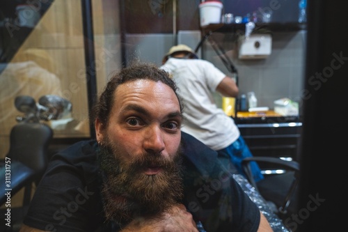 Bearded man with a surprise and emotional expression while a tattoo artist make him a tattoo with a bamboo stick in Bangkok (Thailand) photo