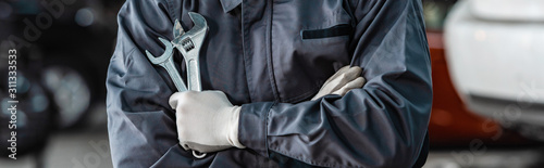 cropped view of mechanic holding wrenches while standing with crossed arms photo