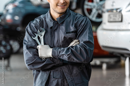 Fényképezés cropped view of smiling mechanic standing with crossed arms and holding wrenches
