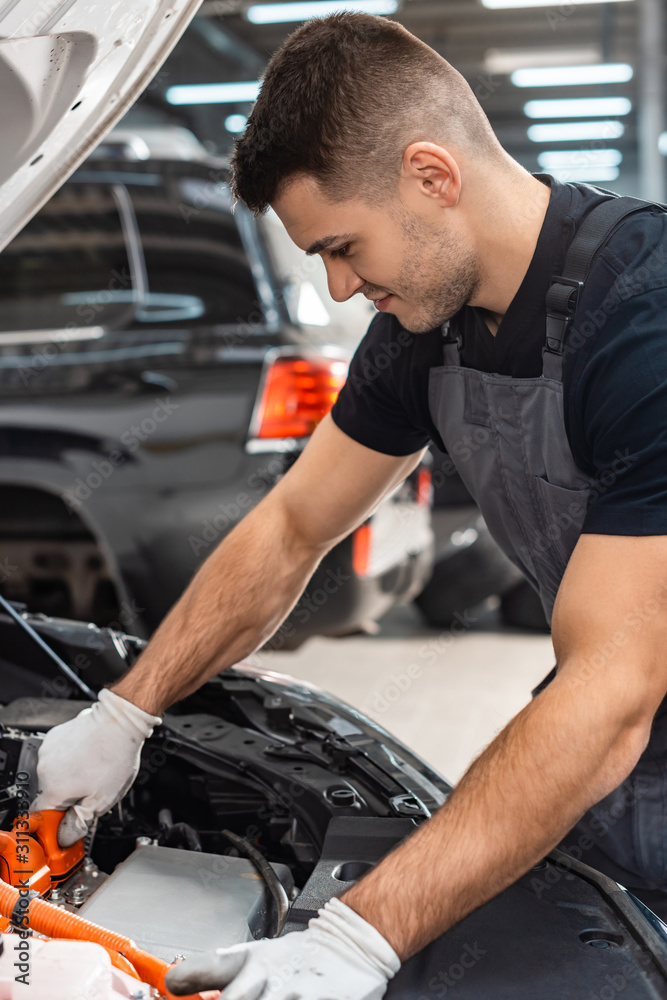 young, smiling mechanic inspecting car engine compartment