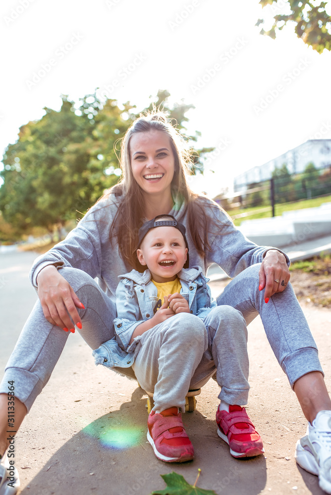 Fototapeta premium Happy family woman mom and little boy son, play and have fun, autumn day on street in city park. Emotions of joy of fun relaxation weekend. Casual warm clothes denim t-shirt. Caring love family.