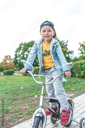 Little boy 3-5 years old, learning to ride bike, autumn day, casual warm clothes. Denim with baseball cap. Driving lessons, first experience, outdoor sports.
