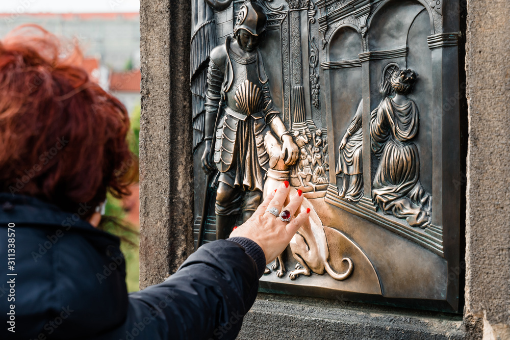 A woman strokes a dog st. Nepomuk bas-relief for good luck on Charles Bridge in Prague. The concept of tourist traditions.