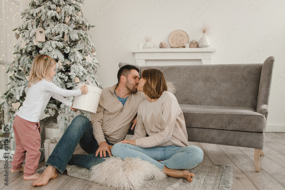Family Christmas morning in a bright minimalistic living room near the Christmas tree.