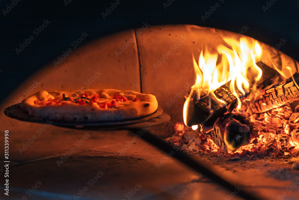 Pizza in the oven on a shovel near the burning wood