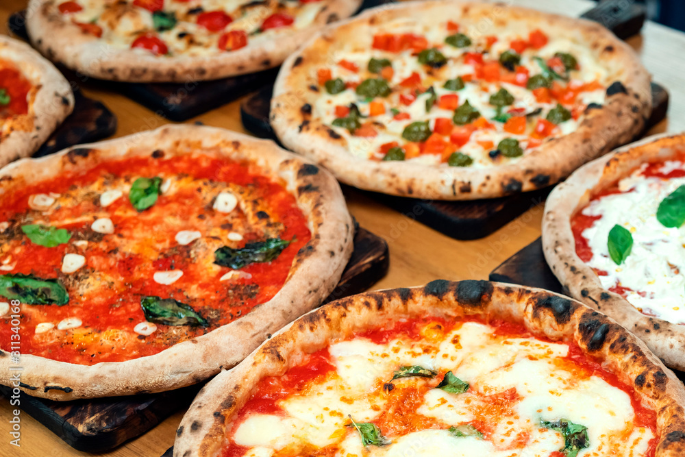 A lot of different freshly prepared pizza on a wooden table in an Italian restaurant A lot of different freshly prepared pizza on a wooden table in an Italian restaurant