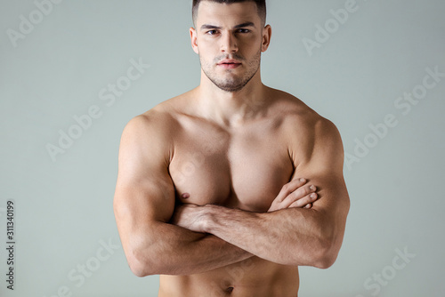 sexy muscular bodybuilder with bare torso posing with crossed arms isolated on grey photo