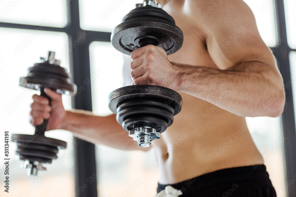 partial view of sexy muscular bodybuilder with bare torso exercising with dumbbells partial view of sexy muscular bodybuilder with bare torso exercising with dumbbells