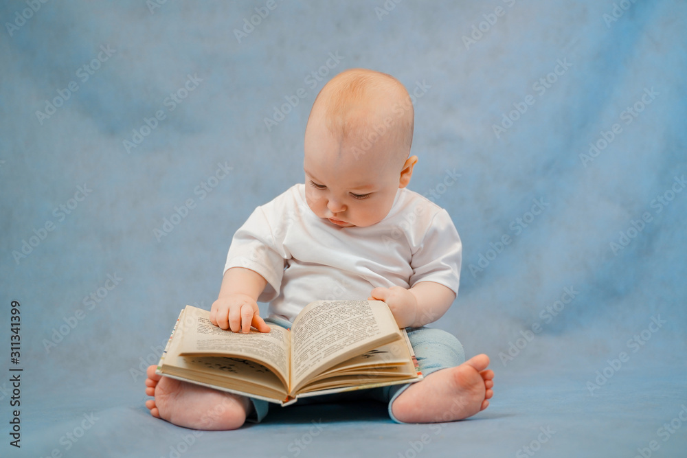 Cute little toddler in light clothes curiously leafs through an old book on a clear blue background. Education concept Cute little toddler in light clothes curiously leafs through an old book on a clear blue background. Education concept
