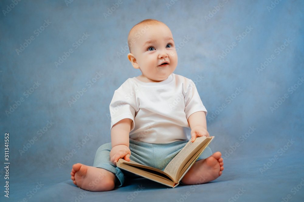 Cute little toddler in light clothes curiously leafs through an old book on a clear blue background. Education concept Cute little toddler in light clothes curiously leafs through an old book on a clear blue background. Education concept
