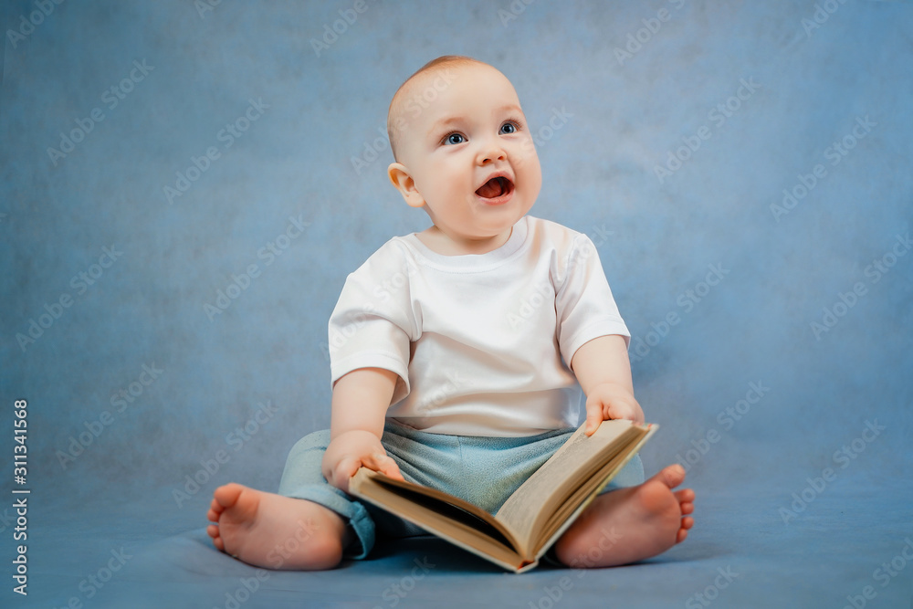 Cute little toddler in light clothes curiously leafs through an old book on a clear blue background. Education concept Cute little toddler in light clothes curiously leafs through an old book on a clear blue background. Education concept