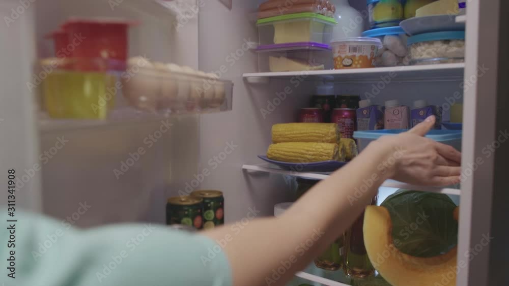 Open fridge full of food. The camera rises and the female hand places a