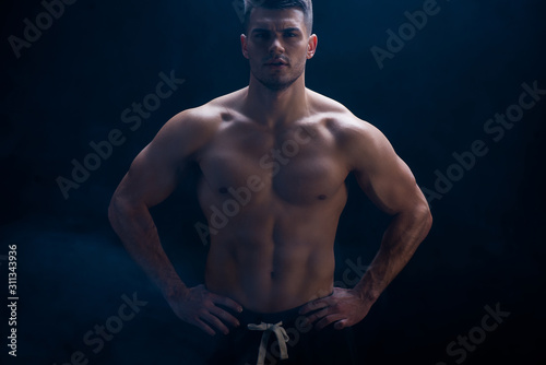 sexy muscular bodybuilder with bare torso posing with hands on hips on black background