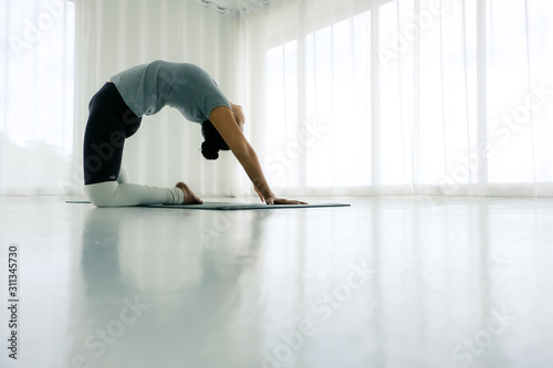 Fototapeta Naklejka Na Ścianę i Meble -  Asian woman practicing yoga in the white room, stretching in Ustrasana exercise, Camel pose, working out, ,Full length Concept of healing body and spirit,copy space