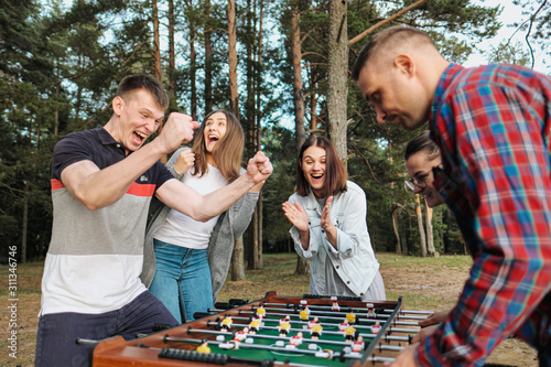 Friends play table football or kicker outdoors. Players and fans rejoice in the victory.