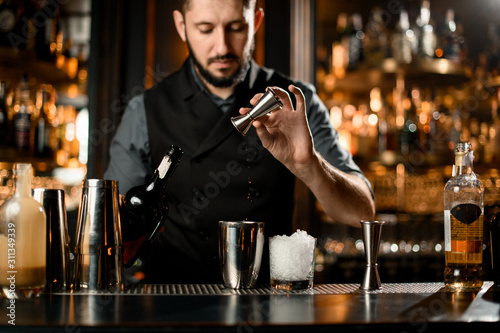 Male bartender pouring a liqour from the jigger to a steel shaker