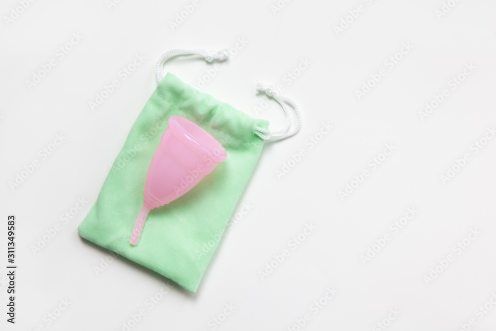 Pink menstrual cup on green small bag on white background. Concept zero waste, savings, minimalism, these days. Feminine hygiene product, flat lay, copy space. Horizontal Pink menstrual cup on green small bag on white background. Concept zero waste, savings, minimalism, these days. Feminine hygiene product, flat lay, copy space. Horizontal