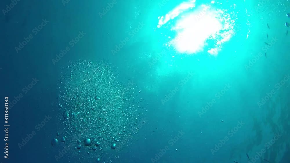 Air bubbles underwater sea rising to water surface, natural scene.sun rays in deep blue tropical sea