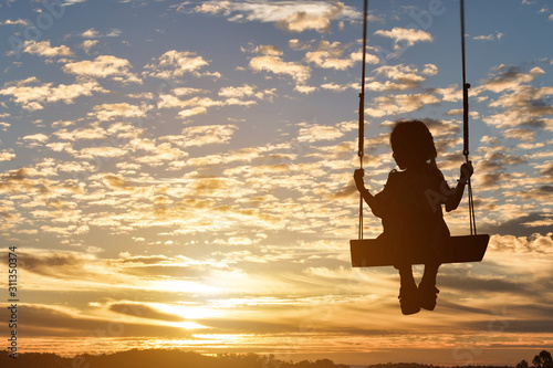 Silhouette of child girl is swing in sunset background.