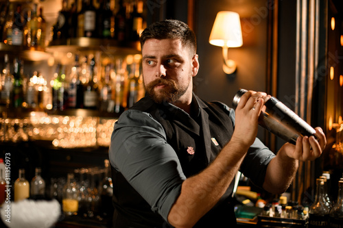 Male bartender holding in hands a steel shaker with a cocktail ready to shake it in the bar