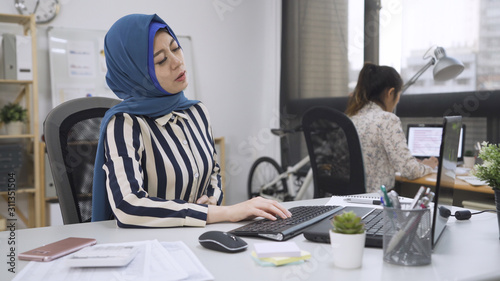muslim business woman with abdominal pain at bright modern workplace in multi ethnic office. arabic worker having painful stomachache working on laptop computer. Body And Health Care Concept. © PRPicturesProduction