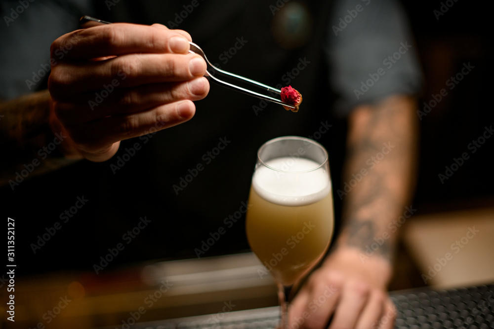 Professional bartender decorated the yellow creamy color alcoholic cocktail drink with a little rose bud
