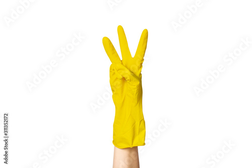 A female hand in a yellow rubber glove for cleaning shows a gesture on a white isolated background. Three fingers