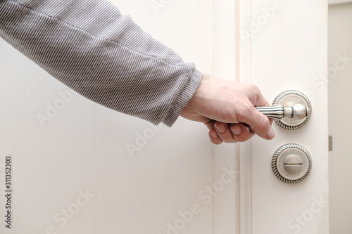 Human hand holding on to a beautiful carved, metal handle in an open wooden door, painted in white color.