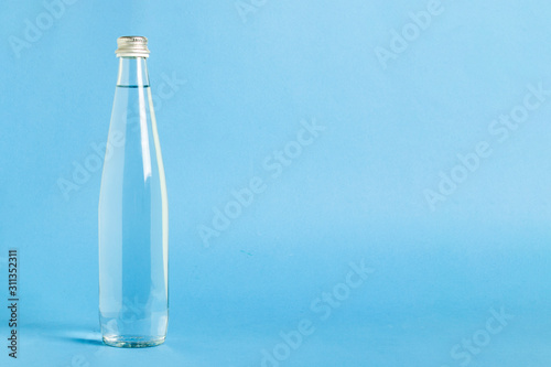 Glass bottle with crystal clear refreshing water on a blue background. Concept of beauty and health, water balance, thirst, summer
