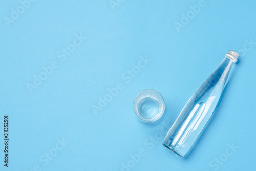Glass bottle and glass with clear water on a blue background. Concept of health and beauty, water balance, thirst, heat, summer. Flat lay, top view