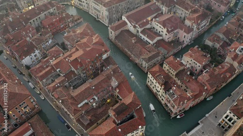 Aerial, tilt, drone shot following a white boat on a small channel, on a sunny evening, in Venice city, Italy photo