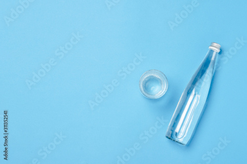 Glass bottle and glass with clear water on a blue background. Concept of health and beauty, water balance, thirst, heat, summer. Flat lay, top view