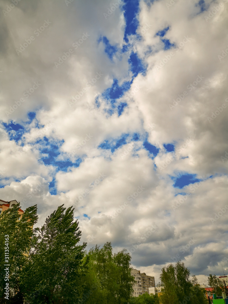 Big white Cumulus clouds over a city of apartment buildings and tall green trees