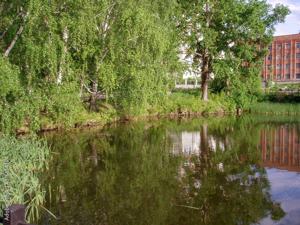 City Park with green trees drooping branches to the lake and a red building in the background City Park with green trees drooping branches to the lake and a red building in the background