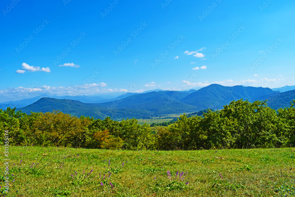 Green mountains and blue sky. Beautiful summer landscape with multilayered hills and forest. Horizontal photo. Main Caucasian ridge, Adygea, Russia.