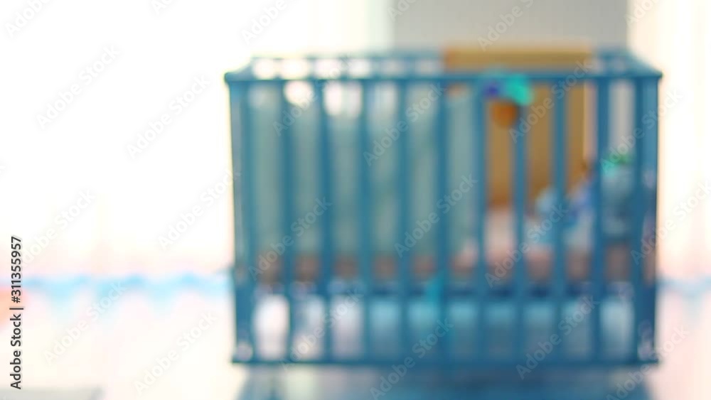 Out of focus of a small kid, child in a wooden baby cot, playing. Lonely. Alone. In the room. Some toys in front of cot. Out of focus of a small kid, child in a wooden baby cot, playing. Lonely. Alone. In the room. Some toys in front of cot.