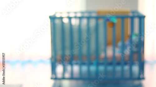 Out of focus of a small kid, child in a wooden baby cot, playing. Lonely. Alone. In the room. Some toys in front of cot.
