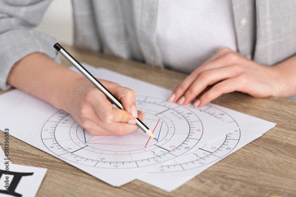 Cropped view of astrologer drawing natal chart on wooden table Cropped view of astrologer drawing natal chart on wooden table
