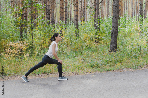 Attractive woman in sports clothes doing sports exercises on the road, loves gymnastics, stretching her legs. An active young girl is engaged in sports, leads a healthy lifestyle in the Park outdoors.