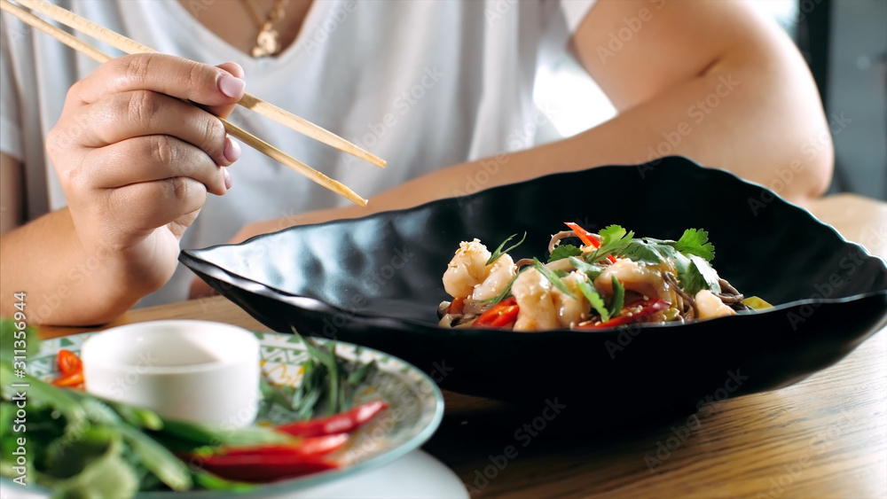 Woman eating traditional asian soba stir-fry noodles with shrimp at restaurant, close-up. Asian food concept.
