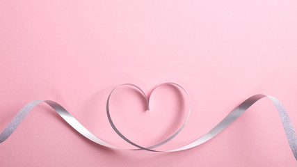Heart shape border made of silver ribbon on pink background. Greeting card mockup for Valentine's Day or birthday, Mother's day. Love concept. Flat lay, top view.