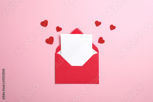 Red paper envelope with blank white note mockup inside and Valentines hearts on pink background. Flat lay, top view. Romantic love letter for Valentine's day concept.