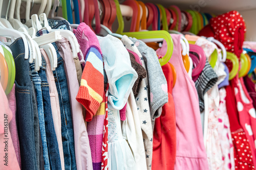 Large selection of bright, children's clothes for a girl hanging in a closet, on hangers.