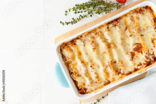 Cannelloni pasta with filling of ground beef, tomatoes, baked with bechamel tomato sauce and mozzarella. Classical Italian cuisine, white tablecloth with embroidery, rustic style, top view, copy space