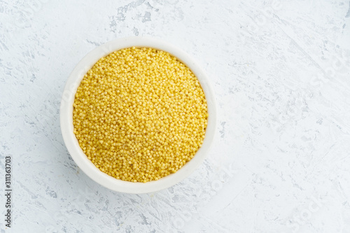 Millet, bulrush in white bowl on white background. Lectine free, dried cereals in cup, vegan food, fodmap diet. Top view, close up. photo