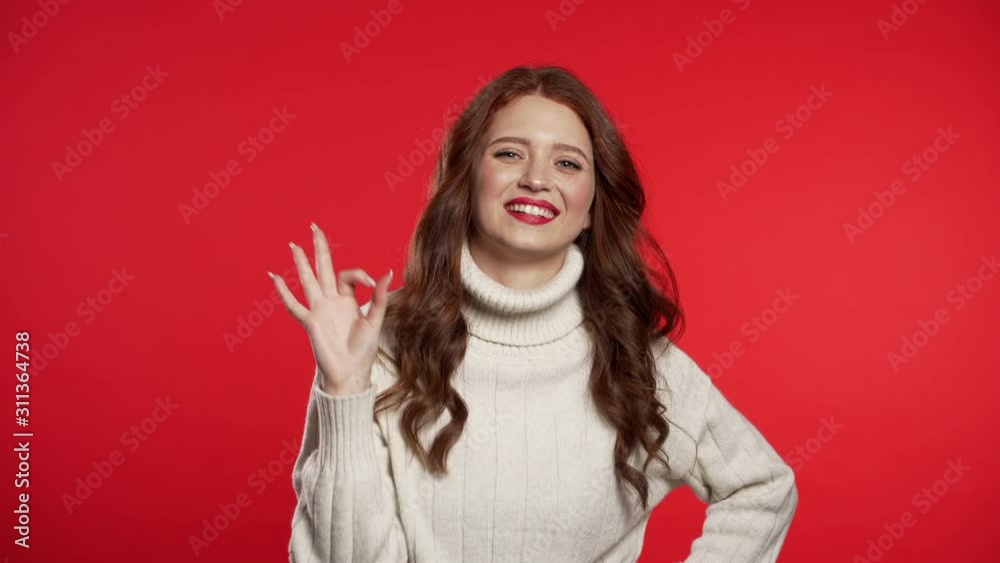 Young woman with perfect make-up making OK sign over background. Winner. Success. Positive girl smiles to camera. Body language. Young woman with perfect make-up making OK sign over background. Winner. Success. Positive girl smiles to camera. Body language.