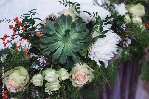 marriage flower composition with succulent, chrysanthemum, rose, pistachio, thuja, waxflower, ilex, pine cones on table for winter wedding indoors, close-up stock photo image